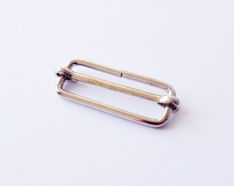 May include: Silver metal slider buckle for adjusting the length of straps or belts.
