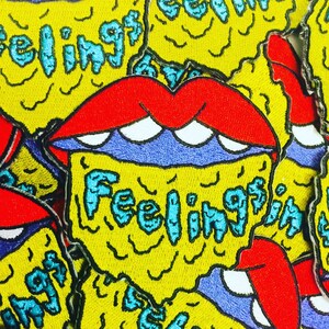 May include: Close-up of a yellow, red, and blue embroidered patch with the word "Feelings" in a dripping font.