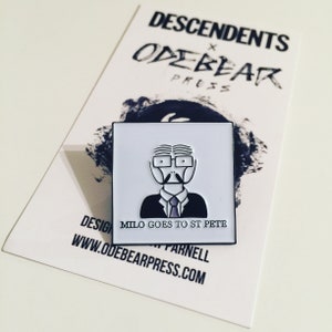 May include: White enamel pin featuring a cartoon illustration of a man with glasses and a mustache. The text "Milo Goes to St Pete" is printed below the illustration.