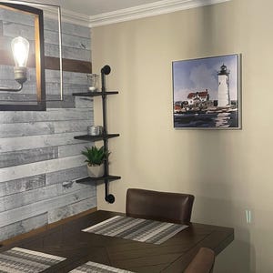 May include: A brown wooden dining table with three placemats and two chairs. The table has a chevron pattern. A painting of a lighthouse is hanging on the wall behind the table.