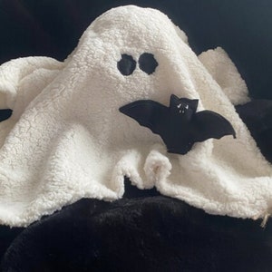 May include: A white plush ghost with black eyes and a black felt bat attached to it. The ghost is sitting on a black fuzzy surface. The text "Successfully Adopted" is written above the ghost.