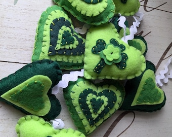 May include: A garland of eight green felt hearts with shamrock designs. The hearts are sewn together with white ribbon.