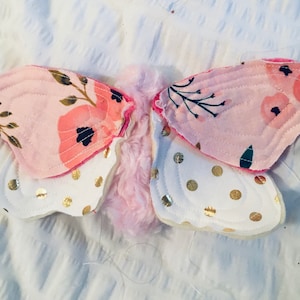 May include: Pink and white butterfly wings with floral and polka dot patterns. The wings are made of fabric and are sewn together.