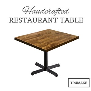 May include: Handcrafted restaurant table with a brown wood top and a black metal base. The table has a square top and a cross-shaped base.