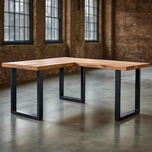 May include: L-shaped wooden desk with a light brown finish. The desk has black metal legs. The desk is in a room with brick walls and large windows.