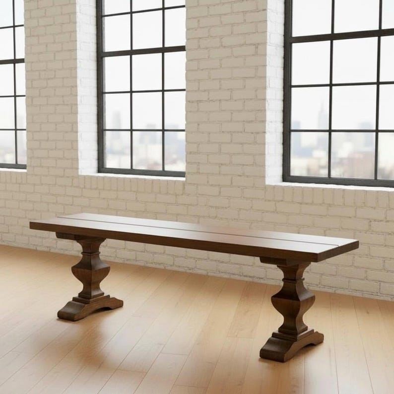 May include: A long, rectangular wooden bench featuring a smooth, dark brown finish. The bench is supported by two ornate, pedestal-style legs with a carved, bulbous design that tapers toward the base, providing a stable foundation for the seat.