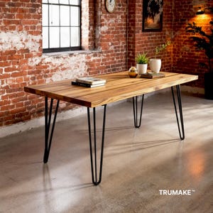 May include: A wooden dining table with a natural wood finish and black hairpin legs. The table is set on a concrete floor in a loft-style room with exposed brick walls.