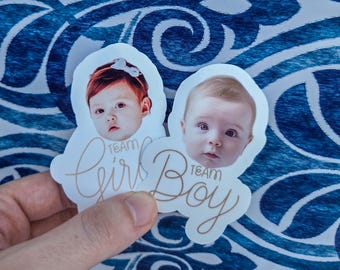 May include: Two die-cut stickers featuring photographic portraits of infants. One sticker displays a baby with a white bow and the text Team Girl in gold script. The second sticker shows a baby with the text Team Boy in gold script below the face.