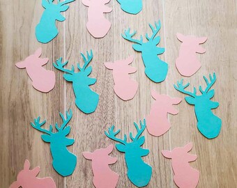 May include: A collection of teal and pink paper deer head cutouts. The deer heads are arranged in a random pattern on a wood surface.