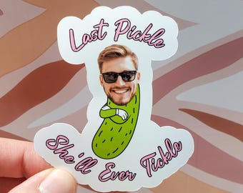 Könnte beinhalten: Ein weißer Aufkleber mit einem grünen Gurken-Design, das das Gesicht eines lächelnden Mannes mit Sonnenbrille integriert. Der Aufkleber hat einen rosa Text, der "Last Pickle She'll Ever Tickle" lautet.