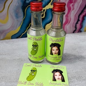 May include: Two small glass bottles with red caps and green labels. One label says "Last Pickle" with a cartoon pickle wearing sunglasses. The other says "Elizabeth's Bachelorette Party 10-15-2025". A matching card is below.
