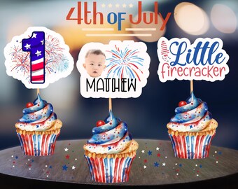 Könnte beinhalten: Drei Cupcakes mit roter, weißer und blauer Glasur und Dekorationen. Jeder Cupcake hat einen dekorativen Aufsatz. Einer sagt "1" mit Feuerwerk, ein anderer hat das Gesicht eines Babys und den Namen "Matthew", und der letzte sagt "Little firecracker". Die Worte "4th of July" stehen oben.