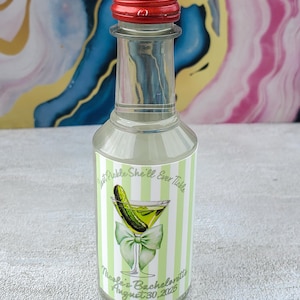 May include: A clear glass bottle with a red cap, featuring a label with a pickle martini graphic and text. The label reads "Just Pickle She'll Ever Tickle" and "Nicole's Bachelorette August 30, 2025". The bottle has a green and white striped background.