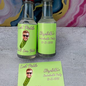 May include: Two small glass bottles with red caps and green labels that read "Last Pickle" and "Elizabeth's Bachelorette Party 10-13-2026". A matching card is below the bottles.