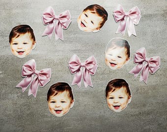 May include: Seven pink bows with a baby face in the center of each bow. The baby faces are all smiling.