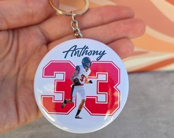 May include: A round keychain with a football player image. The keychain has a white background with the name "Anthony" in cursive and the number "33" in red. The player is wearing a helmet and uniform.