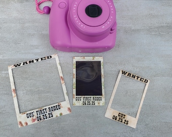 May include: A pink instant camera sits above three photo frames. Two frames read "WANTED" and "GUS' FIRST RODEO 06.25.25". The third frame has a black photo with a cactus and cowboy boot pattern.