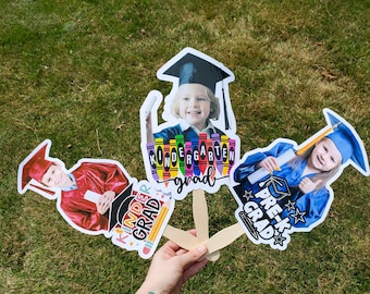 Könnte beinhalten: Drei Foto-Requisiten für den Abschluss auf Holzstäben. Einer sagt "Kinder Grad" mit einer Bleistiftgrafik, ein anderer sagt "Kindergarten grad" mit Buntstiftgrafiken und der letzte sagt "Pre-K Grad" mit Sterngrafiken.