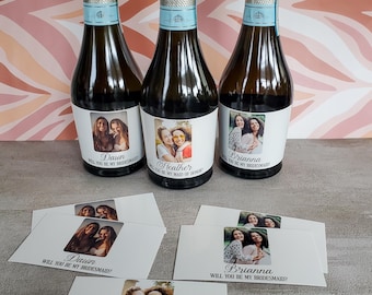 Könnte beinhalten: Drei Champagnerflaschen mit silbernen Folienverschlüssen und Etiketten mit Fotos und Namen. Die Etiketten lauten "Dawn, Will You Be My Bridesmaid?", "Heather, Will You Be My Maid of Honor?" und "Brianna, Will You Be My Bridesmaid?".