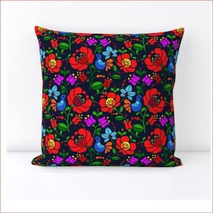 以下が含まれることがあります： 花柄の装飾的な枕。枕には、濃い青色の背景に、赤、黄、青、緑、ピンクの花が描かれています。花は様式化されており、フォークアートのような雰囲気があります。