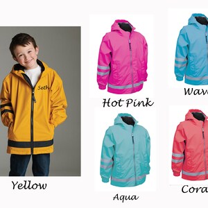 May include: Five children's rain jackets in different colors: yellow, hot pink, blue, aqua, and coral. Each jacket has reflective strips on the sleeves and a hood. The yellow jacket has the name "Seth" embroidered on the front.