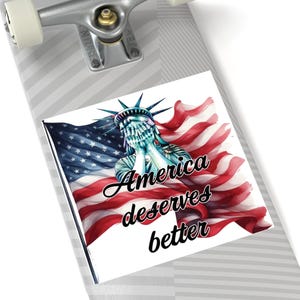 May include: A sticker with the Statue of Liberty, hands covering her face, against a waving American flag. The text "America deserves better" is written in a cursive font.