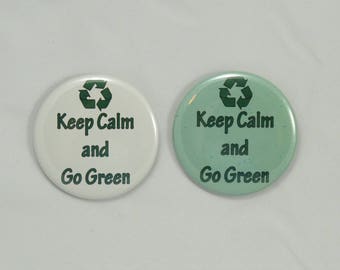 Könnte beinhalten: Zwei runde Knöpfe mit dem Text "Keep Calm and Go Green" und einem grünen Recycling-Symbol. Ein Knopf ist weiß und der andere hellgrün.