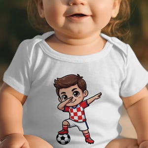Baby wearing white bodysuit with cartoon soccer player doing a dab.