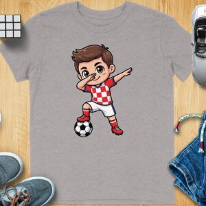 Boy in Croatian soccer uniform dabbing next to a soccer ball.