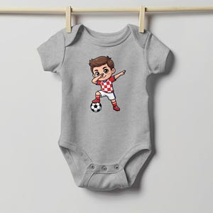 Baby bodysuit with a cartoon boy dabbing over a soccer ball.
