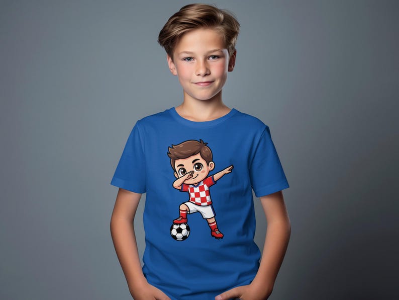 Boy wearing blue t-shirt with cartoon soccer player dabbing, standing by a soccer ball.