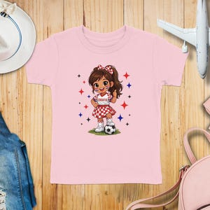 Pink t-shirt with cartoon girl in Croatian flag outfit holding a soccer ball.