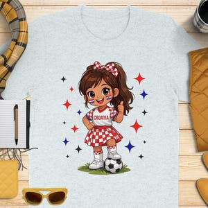 Child in Croatia soccer uniform giving thumbs up next to soccer ball.