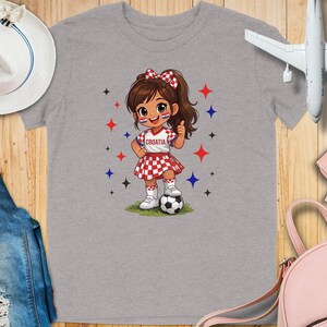Cartoon girl in Croatia soccer uniform with ball, thumbs up.