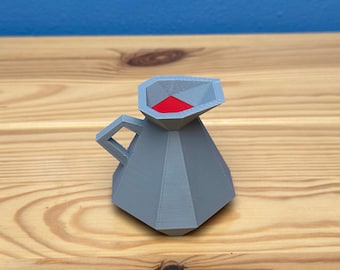 May include: A small, grey, geometric jug with a red interior. The jug has a handle and a pointed spout.