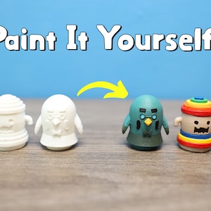 Puede incluir: Cuatro figuritas sin pintar, dos blancas, una turquesa y una con un patrón de arcoíris, listas para ser pintadas. El texto "Paint It Yourself!" está sobre las figuritas.