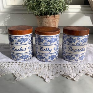 May include: Three ceramic spice jars with wooden lids. The jars are decorated with a blue and white floral pattern. The labels on the jars read "Muskat", "Curry", and "Paprika".