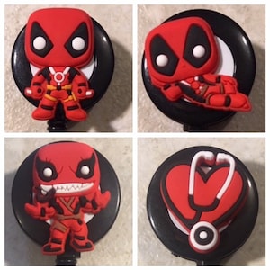 May include: Four different badge reel designs. The first two feature a red and black Deadpool character. The third features a red and black Venom character. The fourth features a red heart with a stethoscope.