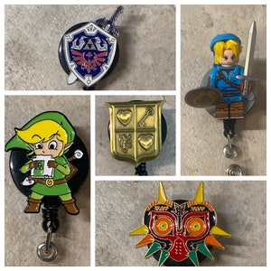 May include: A set of five different Nintendo themed retractable badge holders. The holders feature a gold shield with hearts and a key, a gold and black Triforce shield, a gold and black Majora's Mask, a gold and black Link character, and a gold and black Link character holding a Nintendo game cartridge.