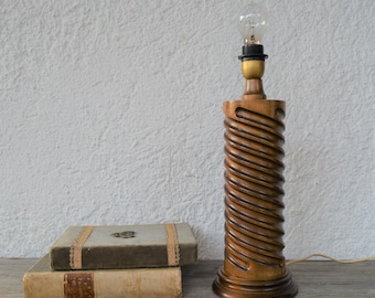 May include: A wooden table lamp with a spiral design. The lamp has a brown finish and a clear glass bulb. The lamp is sitting on a wooden table next to two books.