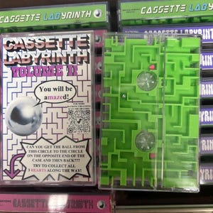 May include: A green Cassette Labyrinth puzzle game with a clear plastic cover. The game features a maze design with a metal ball and the text "CASSETTE LABYRINTH VOLUME II". The packaging includes the text "You will be amazed!" and instructions.