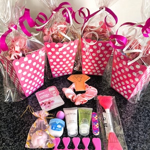 May include: Pink and white polka dot favor boxes filled with various beauty products, including hair ties, face masks, and hand cream. The boxes are wrapped in clear cellophane and tied with pink ribbon.