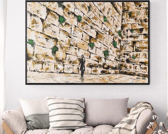 Könnte beinhalten: Abstrakte Malerei der Klagemauer in Jerusalem, mit einer strukturierten, beigefarbenen Steinmauer und grünen Akzenten. Eine Figur steht vor der Mauer. Das Kunstwerk ist schwarz gerahmt und hängt über einem Sofa.