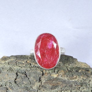 May include: A silver ring featuring a large, oval-shaped, red ruby gemstone.