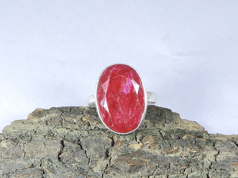 May include: A silver ring featuring a large, oval-shaped, red ruby gemstone.