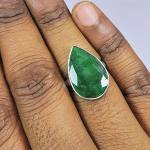 May include: A silver ring with a large, teardrop-shaped emerald gemstone.