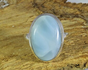 Könnte beinhalten: Ein silberner Ring mit einem hellblauen ovalen Edelstein. Der Ring liegt auf einer Holzoberfläche.