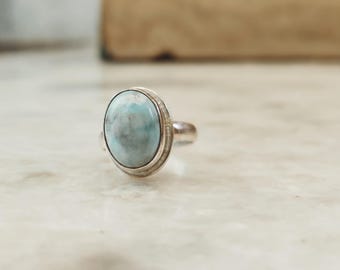 May include: A silver ring with a light blue oval-shaped gemstone set in a silver bezel.