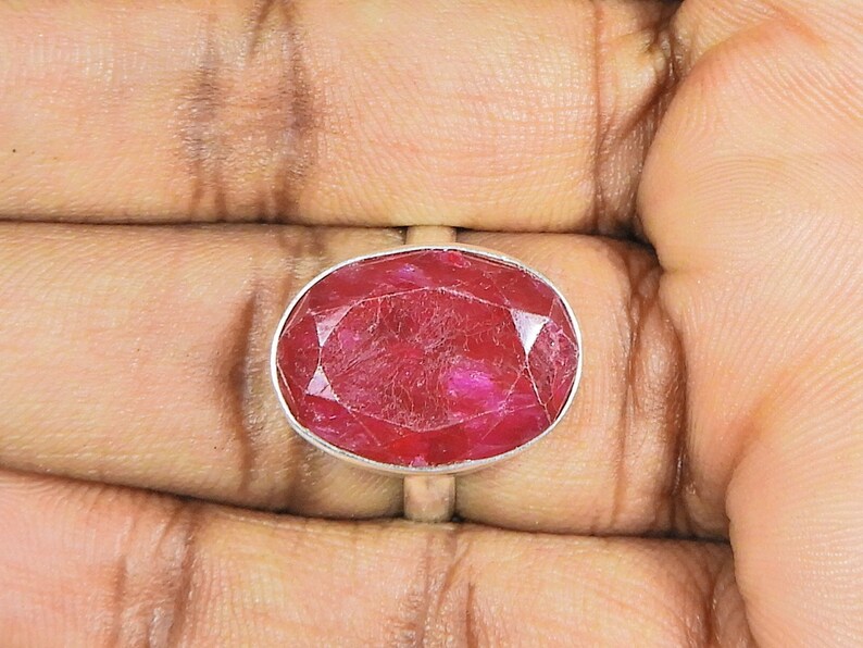 May include: A silver ring featuring a large, oval-shaped, red ruby gemstone.