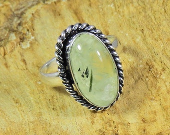 May include: A silver ring with a green and white oval gemstone set in a rope-like design.